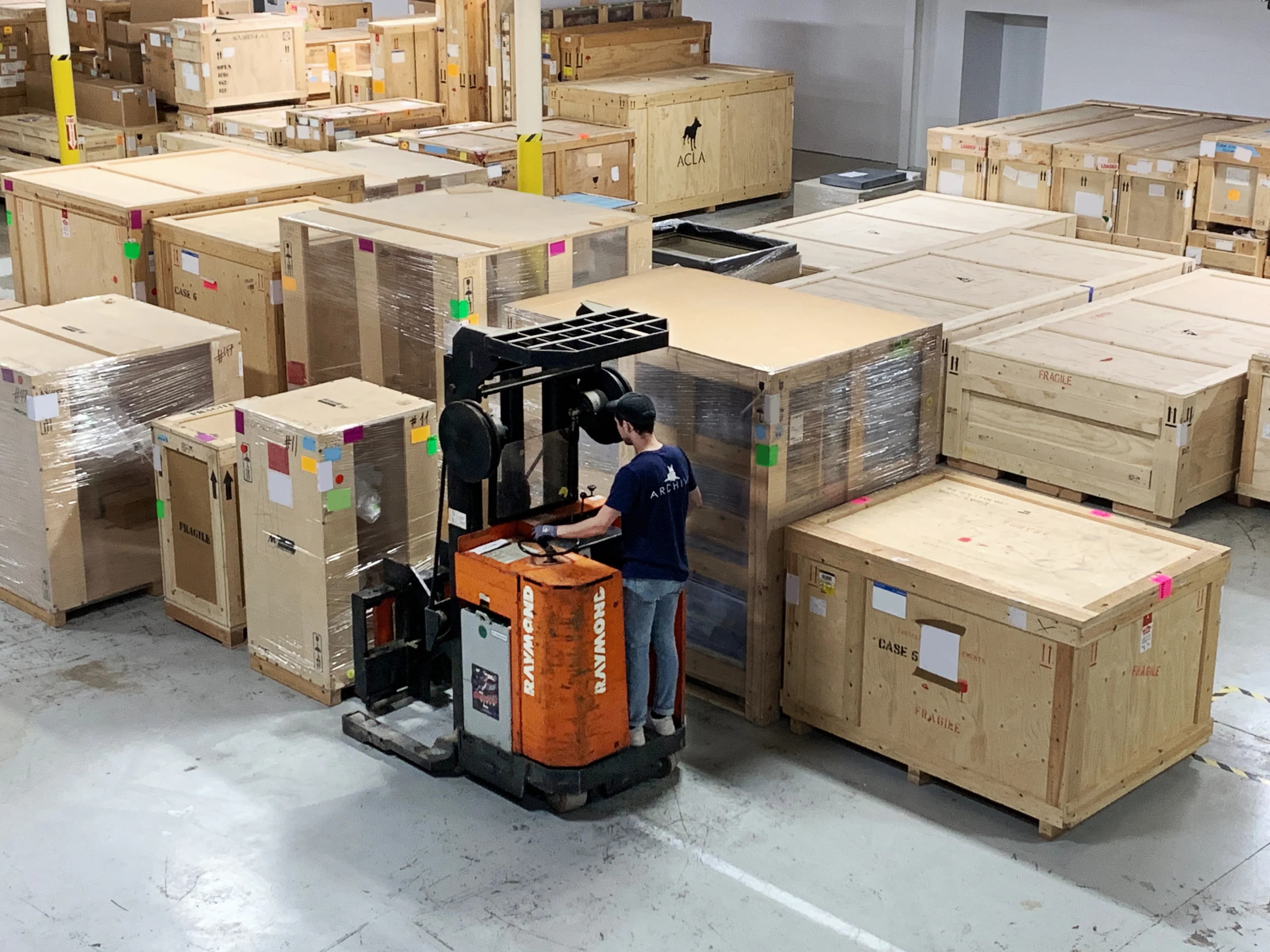 Forklift operator navigating rows of wooden crates in warehouse