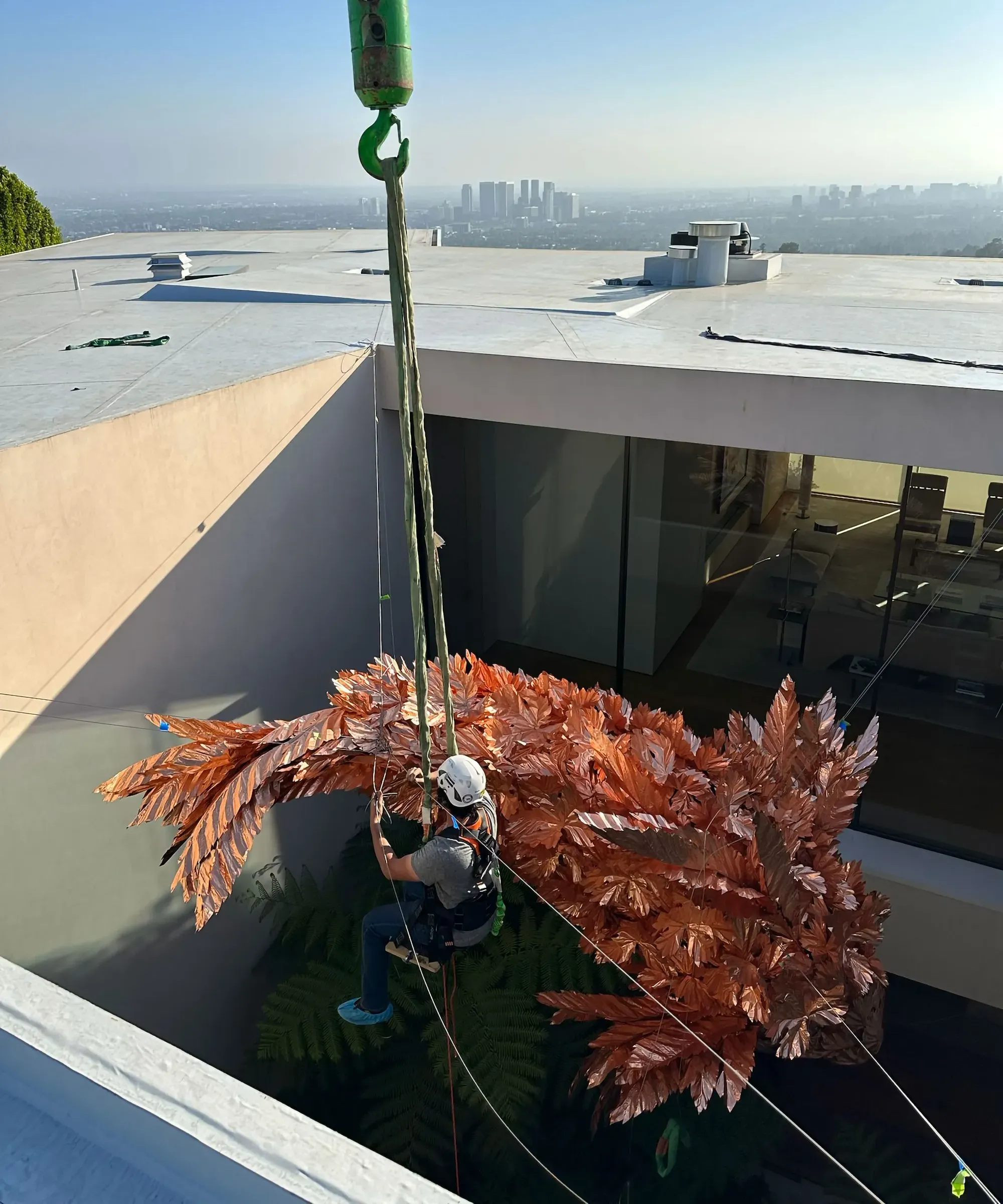 Crane lowering copper leaf sculpture into building courtyard